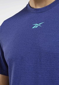 Sportovní tričko s krátkými rukávy v tmavě modré barvě s texturovaným vzorem. Na hrudi je tyrkysové logo a má kulatý výstřih.