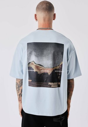 Camiseta de gran tamaño en azul claro con una gran impresión gráfica negra de montañas y texto en la parte posterior. Mangas cortas, material de algodón.