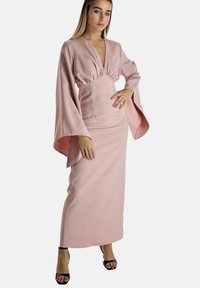 Długa, różowa sukienka z głębokim dekoltem w serek, marszczonym stanem i powiewającymi rękawami w kształcie dzwonów, wykonana z gładkiej, satynowej tkaniny. Noszona z czarnymi szpilkami.