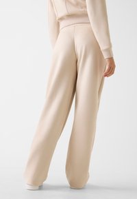 Pantalon de survêtement beige à jambes larges en tissu doux et texturé. Doté d'une taille haute et d'ourlets retroussés. Les coutures apportent un intérêt subtil.