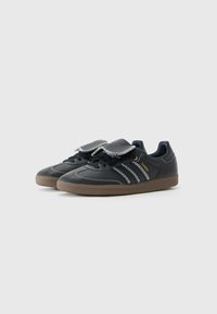 Sorte skinnesneakers med lav profil, som har borrelåsrem, hvit søm og tre sidestreker. Gummisåle med en teksturert overflate.
