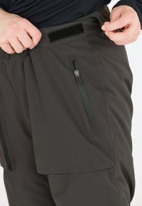 Grijze outdoorbroeken met een gestructureerde afwerking, voorzien van een ritszak aan de zijkant, drukknopen en een klittenbandsluiting op de tailleband.