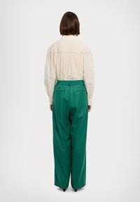 Pantaloni larghi verdi con cintura elasticizzata e due tasche posteriori, abbinati a una blusa lunga a maniche corte color crema con texture.