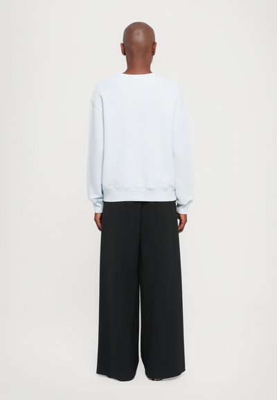 Lys blå genser med lange ermer og avslappet passform, parret med vide svarte bukser. Glatt stoff og avslappet silhuett.