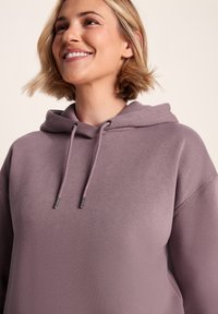 Light purple hoodie with a relaxed fit, featuring a drawstring hood and metallic accents. Soft texture, smooth material, and minimal design.