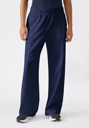 Osoba nosząca granatowe spodnie z szerokimi nogawkami i elastycznym pasem oraz czarno-biały sportowy obuwie na białym tle.