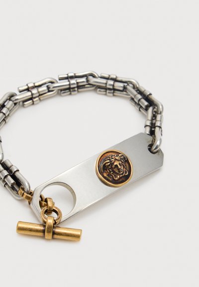 Ασημένιο και χρυσό βραχιόλι αλυσίδας με ορθογώνια μεταλλική πλακέτα που φέρει χρυσό έμβλημα κεφαλής Μέδουσας και χρυσό κούμπωμα τύπου toggle.