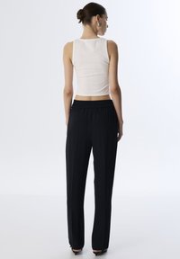Biała bezrękawnikowa bluzka o dopasowanym kroju, zestawiona z czarnymi spodniami o wysokim stanie, posiadającymi marszczony pas i prostą nogawkę.