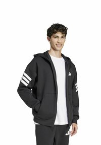 Felpa nera con zipper realizzata in morbido tessuto, con cappuccio, ampie tasche anteriori e tre strisce bianche su entrambe le maniche.