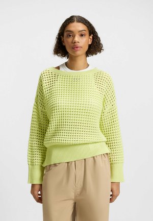 Strickpullover in leuchtendem Limettengrün mit Lochmuster, gerippten Bündchen und Saum, strukturiertem Stoff und lässigem Schnitt. Stylisch kombiniert mit beigen Hosen.