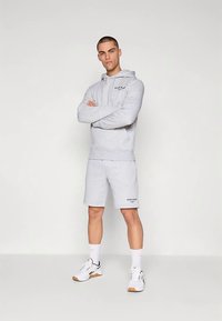 Grå bomulls-hoodie med framficka, kombinerad med matchande shorts. Har en logotyp på bröstet och shortsen, kompletterad med vita sneakers.