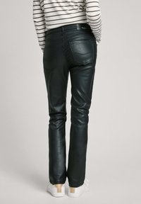 Pantalones de cuero negro con un diseño ajustado, que cuentan con dos bolsillos traseros y detalles de costura mínimos, combinados con zapatillas blancas.