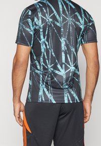 Lyhythihainen urheilupaita, jossa musta pohja ja turkoosi bambukuvio, valmistettu sileästä, kosteutta siirtävästä materiaalista.