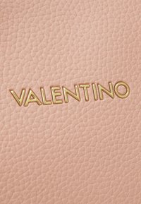 Rosa lädertextur med det präglade guldiga "VALENTINO"-logotypen, som framhäver en slät yta och subtila korniga detaljer.