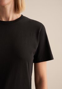 Zwart katoenen T-shirt met een ronde hals en korte mouwen. Zachte textuur, minimalistisch ontwerp, zonder zichtbare patronen of accenten.