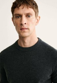 Grauer gestrickter Pullover mit Rundhalsausschnitt. Der Stoff wirkt weich, und die Textur sieht leicht flauschig aus, was ein gemütliches Erscheinungsbild erzeugt.