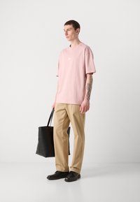 Light pink cotton t-shirt with a crew neck, beige trousers, black leather shoes, and a black tote bag. Simple design, relaxed fit.