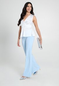 Weißes Satinoberteil mit Peplum-Design, hellblaue ausgestellte Hose, silberne hohe Absätze und eine metallische Clutch. Glatte Texturen und elegante Silhouette.