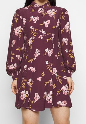Robe bordeaux à imprimé floral, avec des manches longues bouffantes, un col à revers et une évasure à l'ourlet. Le tissu semble léger et lisse.