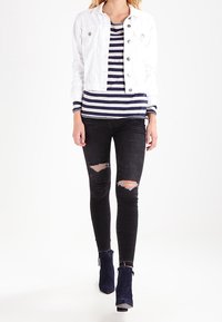 Witte denimjas over een marineblauw en wit gestreept shirt, gecombineerd met zwarte gescheurde skinny jeans en marineblauwe hoge enkellaarzen.