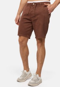 Shorts en coton marron avec une taille à cordon de serrage, des poches latérales et une coupe légèrement décontractée, assortis à des baskets de sport grises.