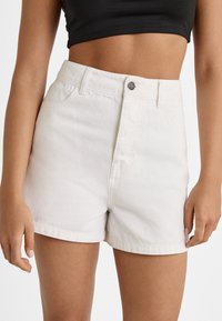 Shorts in denim bianco con vita alta, dotati di tasche anteriori, chiusura a bottone e una texture leggermente usurata.