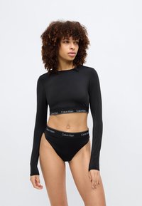 Μαύρο crop top με μακριά μανίκια και λογότυπο Calvin Klein στη μέση, συνδυασμένο με ψηλοτάκουνα μαύρα εσώρουχα με αντίστοιχο λογότυπο.
