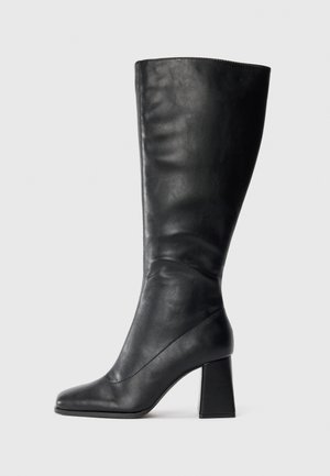 Zwarte leren kniehoogte laars met pointed toe en blokhak voor een effen lichte achtergrond.