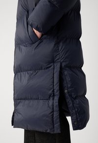 Marineblå puffjakke med en blank finish, med sidelomme og trykknappelukking i kanten. Vattert design med oppblåste seksjoner.