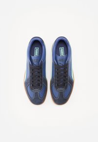 Μπλε σουέτ και δικτυωτά αθλητικά παπούτσια με σχέδιο μαύρων κορδονιών, περφορεσέ, λευκή ραφή και καφέ καουτσούκ σόλα. Branding PUMA στη γλώσσα.