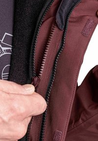 Weinrot Jacke mit einem beidseitigen Reißverschluss mit schwarzen Zähnen, glattem Stoff und einem weichen Innenfutter. Eine Hand zeigt, wie sie den Reißverschluss zieht.