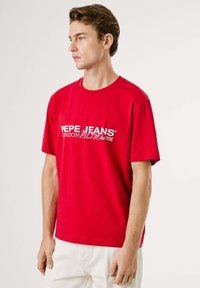 Raudona medvilninė marškinėliai trumpomis rankovėmis, su baltu logotipu "PEPE JEANS LONDON PJL73 Club" per krūtinę. Paprastas apvalios kaklo dizainas.