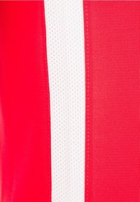 Rode atletische stof met een verticale witte mesh-streep; gladde textuur met een lichte glans. Kenmerkt zich door opvallende stiksels langs de randen.