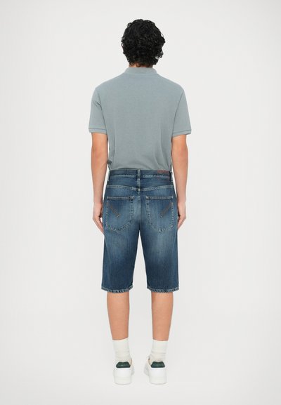 Μπλε τζιν σορτς με δύο πίσω τσέπες, ανοιχτό πλύσιμο και ραφές λεπτομέρειες. Συνδυασμένα με γκρι πόλο μπλούζα και λευκά αθλητικά παπούτσια.