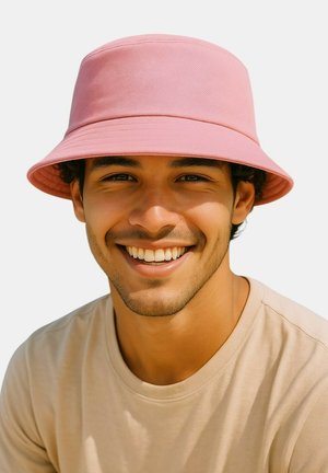 Young man smiling, wearing a light pink bucket hat and beige t-shirt, against a plain white background.