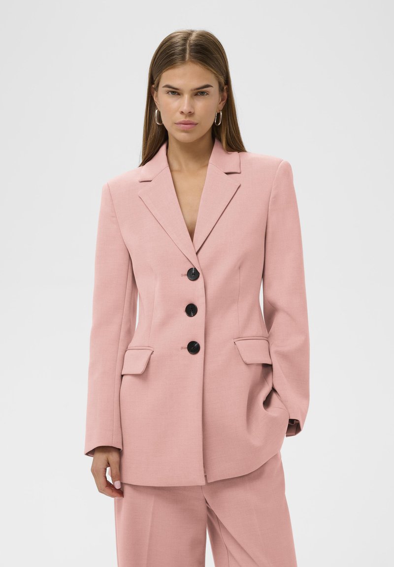 Rosa maßgeschneiderter Blazer mit Kerbkragen, drei schwarzen Knöpfen und Fronttaschen. Glatter Stoff mit einer strukturierten, leicht übergroßen Passform.