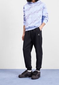 Helle blaue Kapuzenjacke mit lila grafischem Text, schwarze Jogginghose mit weißem Logo und schwarze Sneaker mit strukturierten Details.