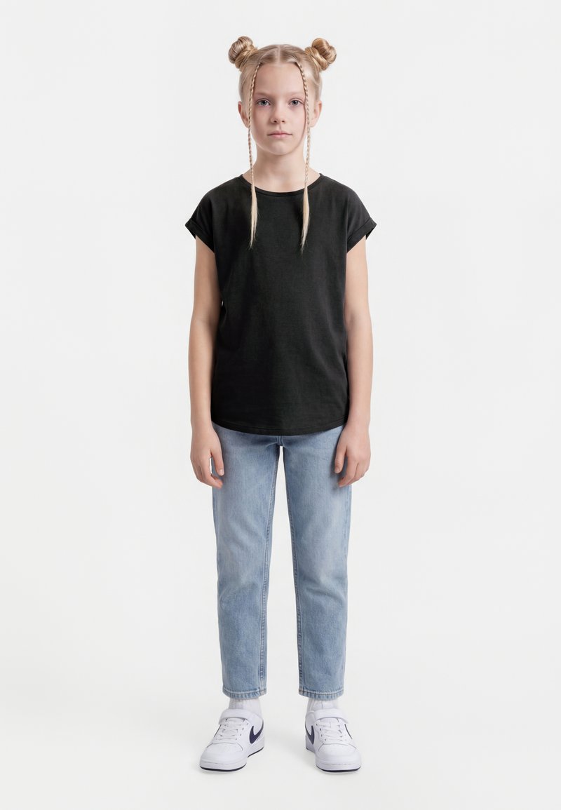 Noor tüdruk seistes, seljas must t-särk, helesinised teksad, valged Nike tossud, kahe punutud kukliga ja kahe esiosa palmikuga.