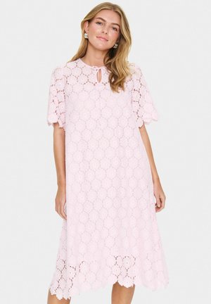 Rochie roz din dantelă cu decolteu rotund, mâneci scurte și tiv ondulat. Prezintă modele florale și un detaliu cu legare în față.