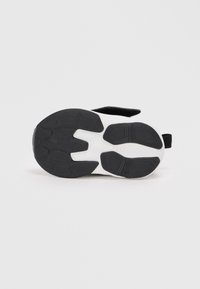 Semelle de chaussure noire en caoutchouc texturé, avec des accents blancs, de forme arrondie et des cannelures flexibles pour la traction et l'adhérence.