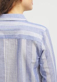 Blau-weiße gestreifte Hemd mit einem Kragen, aus leichtem Stoff, mit einem lässigen Schnitt und sichtbaren Nähten.