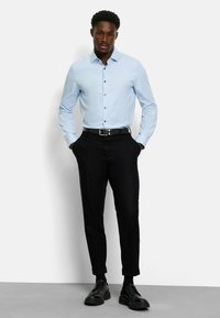 Helles blaues Hemd mit strukturiertem Kragen, kombiniert mit schwarzen, schmal zulaufenden Hosen und schwarzen Schnürschuhen. Einfaches Design, glatte Textur.