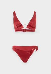 Κόκκινο μπικίνι δύο κομματιών με χρυσούς κρίκους στο κέντρο του πάνω μέρους και στο αριστερό ισχίο, με κούμπωμα στην πλάτη του πάνω μέρους.