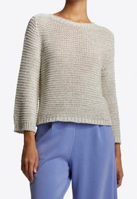 Lichtgrijze gebreide trui met een ronde hals, driekwart mouwen en een textuur van een opengewerkte steek. Gecombineerd met losse, lichtblauwe broek.