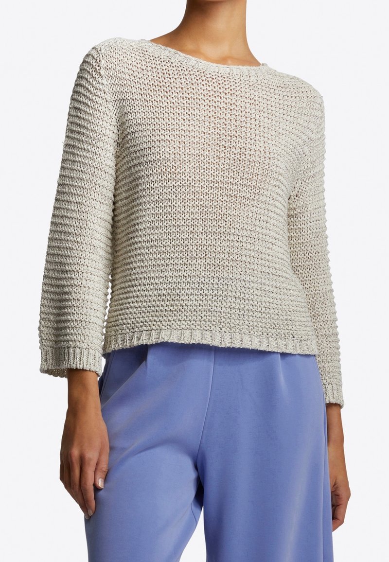 Lichtgrijze gebreide trui met een ronde hals, driekwart mouwen en een textuur van een opengewerkte steek. Gecombineerd met losse, lichtblauwe broek.