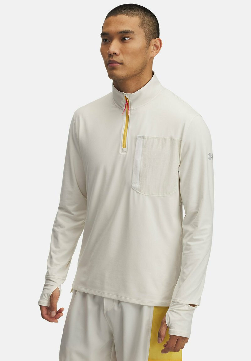 Camicia a maniche lunghe di un leggero colore crema, con una zip frontale a metà. Presenta una tasca sul petto e aperture per il pollice nelle maniche per una maggiore copertura.