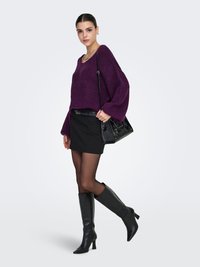 Maglione viola lavorato a maglia con maniche a palloncino, abbinato a una minigonna nera, stivali neri al ginocchio e una borsa nera.