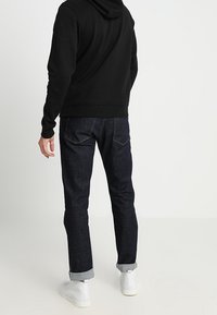 Sudadera negra con capucha, jeans azul oscuro con puños doblados y zapatillas blancas. Tejido suave con un corte estándar y detalles de costura típicos.