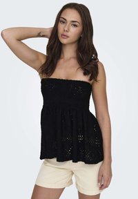 Top noir sans bretelles en dentelle texturée avec une taille froncée, présentant des motifs à œillets. Accompagné de shorts beige clair.