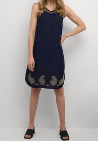 Marineblaues ärmelloses Kleid mit gestickten goldenen Paisleymustern am Saum. Leichter Stoff, gerader Schnitt und runder Ausschnitt.